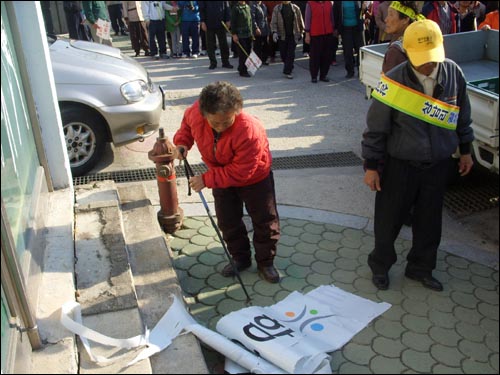 바닥에 떨어진 간판조각을 지팡이로 걷어치우는 할머니의 모습. 